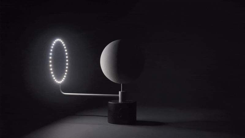 A grayscale animation showing a ring of LED lights rotating around a central spherical moon model on a mechanical arm.